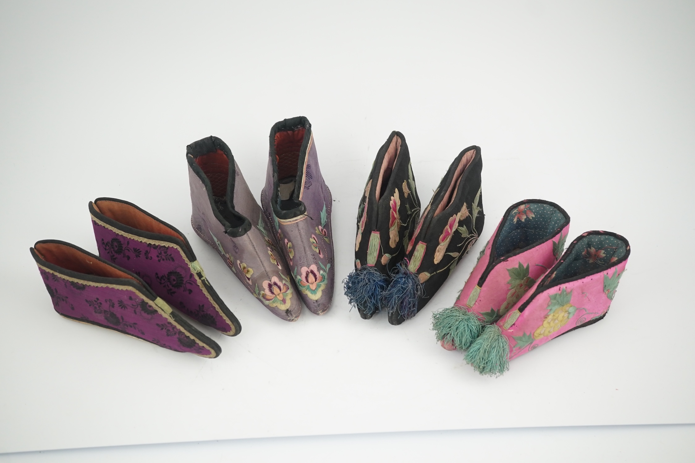 Four pairs of late 19th / early 20th Chinese ladies bound foot shoes, made in various coloured silks, with colourful floral embroidered motifs, two pairs with decorative silk pom-poms and another made of purple and black